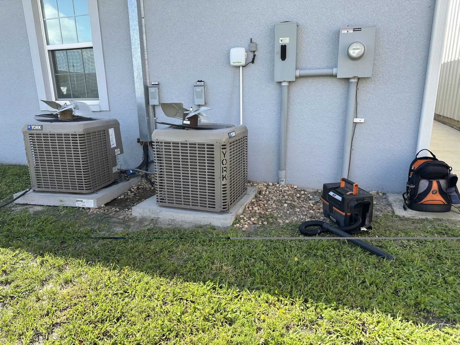 A Temperature Solutions technician inspecting an outdoor AC condenser unit at a residential home in Lakeland, FL during summer. The technician is checking components on a system that has stopped cooling, with a suburban Florida home visible in the background.