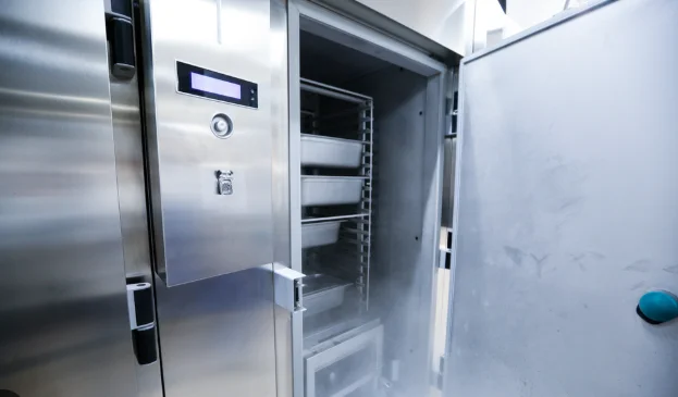 A commercial HVAC technician from Temperature Solutions inspecting the condenser coils on a walk-in cooler unit at a commercial facility in Lakeland, FL. The technician is checking components in a well-lit equipment room typical of food service operations in the area.